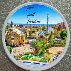 May include: A white round patch with a colorful image of Park Güell in Barcelona, Spain. The text "park güell barcelona" is printed in black on the patch.