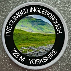 Pode incluir: Etiqueta redonda branca com texto preto e uma foto de uma colina verde. O texto diz "I've Climbed Ingleborough 723 M - Yorkshire".