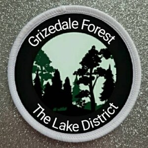 May include: White round patch with black and green design. The text "Grizedale Forest The Lake District" is printed in white on a black background.