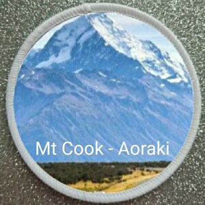 May include: A white circular patch with a blue and white image of a snow-capped mountain peak. The text "Mt Cook - Aoraki" is printed in black at the bottom of the image.