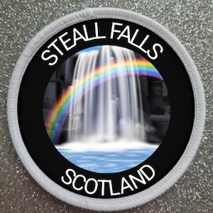May include: A white round patch with black text and a picture of a waterfall with a rainbow. The text reads "Steall Falls Scotland".