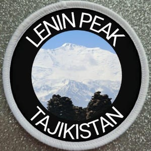 May include: Circular patch with the words "LENIN PEAK TAJIKISTAN" in white. The patch displays a mountain scene with snow-capped peaks and a blue sky, enclosed by a black border.