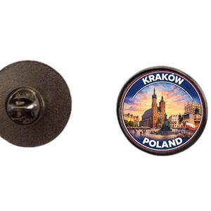 May include: A round pin with a detailed image of Krakow, Poland, featuring a church and cityscape. The pin has a black border and the words "KRAKOW" and "POLAND" are displayed. The pin is shown next to its black pin back.
