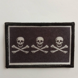 Puede incluir: Parche bordado negro con tres diseños de calavera y huesos cruzados blancos.