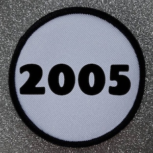 Könnte beinhalten: Runder weißer Patch mit schwarzem Rand und der Jahreszahl 2005 in Schwarz gedruckt.