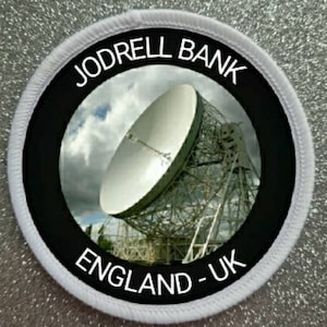 Może przedstawiać: Okrągła naszywka w kolorze białym i czarnym z tekstem "Jodrell Bank England - UK" i czarno-białym obrazem dużego radioteleskopu.