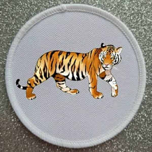May include: A white round iron-on patch with a black outline featuring a detailed illustration of an orange and black tiger walking to the right.