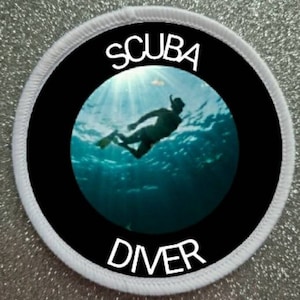Könnte beinhalten: Runder weißer Patch mit schwarzem Rand und einer Silhouette eines Tauchers in einer blauen Ozeanszene. Der Text "SCUBA DIVER" ist in weiß gedruckt.