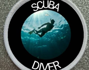 Könnte beinhalten: Runder weißer Patch mit schwarzem Rand und einer Silhouette eines Tauchers in einer blauen Ozeanszene. Der Text "SCUBA DIVER" ist in weiß gedruckt.