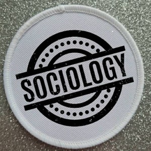 Op de afbeelding: Ronde witte stoffen patch met een zwart-wit distressed cirkelontwerp. De cirkel heeft de tekst "SOCIOLOGY" in zwart gedrukt.