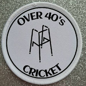 Peut inclure: Écusson rond blanc avec du texte noir et un graphique d'un guichet de cricket. Le texte indique "Over 40's Cricket".