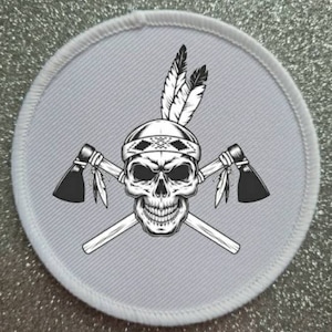 May include: White round patch with a black and white illustration of a skull wearing a headdress with feathers and holding two crossed tomahawks.