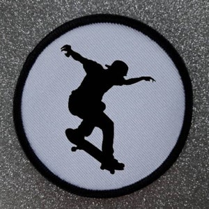 Puede incluir: Silueta en blanco y negro de un patinador haciendo un truco sobre un fondo blanco. La imagen es un parche circular con un borde negro.