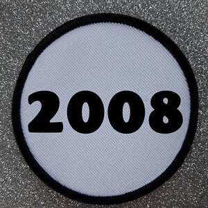 Könnte beinhalten: Runder weißer Patch mit schwarzem Rand und der Zahl 2008 in Schwarz gedruckt.