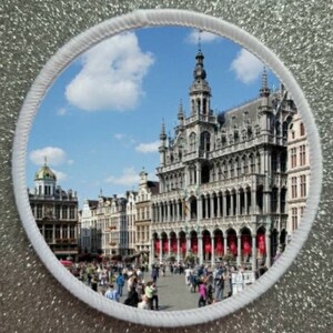 Puede incluir: Una foto circular de la Grand Place de Bruselas, Bélgica. La foto muestra la arquitectura ornamentada de los edificios, incluyendo el Ayuntamiento, con una multitud de personas en primer plano.