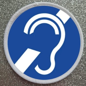 May include: A white circle with a blue background and a white stylized ear with a diagonal line through it. The symbol is used to indicate hearing impairment.