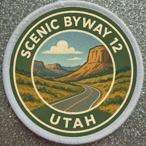 May include: Circular patch with a scenic landscape design. The patch features a road winding through a desert landscape with mountains and a large mesa. The text "SCENIC BYWAY 12 UTAH" is printed around the edge.