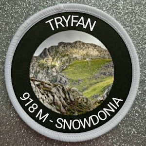 May include: White round patch with a black circle in the center. The circle has a photo of a mountain range with the text "TRYFAW 918 M - SNOWDONIA" around the image.