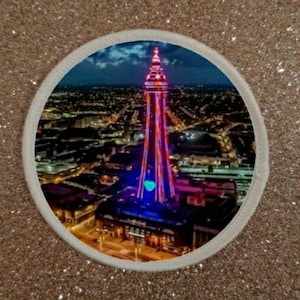 Peut inclure: Vue aérienne nocturne d'une haute tour illuminée avec des lumières roses et bleues. La tour est entourée d'une ville avec de nombreuses lumières.