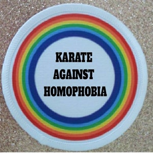 May include: A white round patch with a rainbow border. The centre of the patch has the text "KARATE AGAINST HOMOPHOBIA" in black.