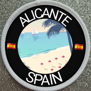 Può includere: Un cerotto rotondo bianco con un cerchio nero al centro. Il cerchio contiene il testo "ALICANTE SPAGNA" in lettere bianche. All'interno del cerchio c'è una scena di spiaggia con palme, barche a vela e ombrelloni rosa. La bandiera spagnola è su entrambi i lati del cerchio.