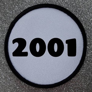 Peut inclure: Patch rond blanc avec une bordure noire et le nombre 2001 imprimé en noir.