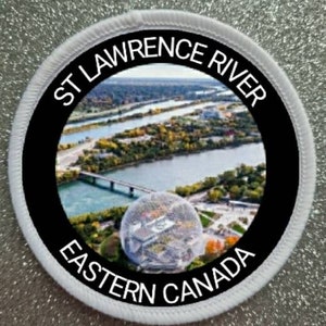 May include: White round patch with black border and text "ST LAWRENCE RIVER EASTERN CANADA". The patch features a photo of a river and a large building with a geodesic dome.