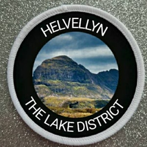May include: White round patch with a black circle in the centre. The black circle has the text "Helvellyn The Lake District" in white lettering around a photo of a mountain.