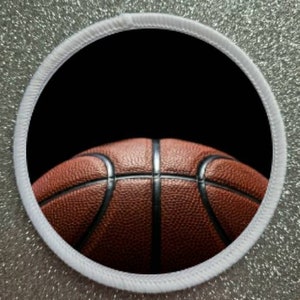 May include: A close-up of a brown basketball with black lines, against a black background. The basketball is partially visible, with the top half of the ball in focus.