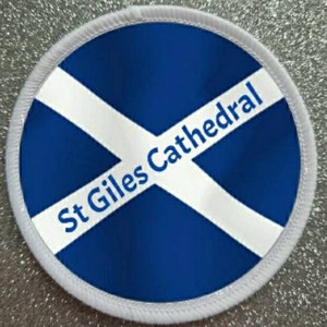 Puede incluir: Parche redondo blanco con fondo azul y una cruz diagonal blanca. El texto "St Giles Cathedral" está escrito en negro sobre la cruz.