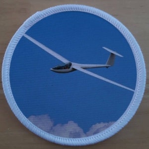 Può includere: Un aliante bianco che vola contro un cielo blu con nuvole bianche sullo sfondo. L'aliante è un tipo di aeromobile popolare utilizzato per il volo ricreativo.