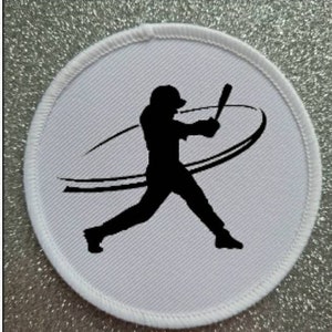 Peut inclure: Patch rond blanc avec une silhouette noire d'un joueur de baseball en train de frapper une balle. Le joueur est en plein swing avec une traînée de mouvement derrière lui.