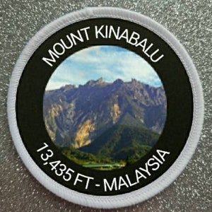Op de afbeelding: Een ronde witte en zwarte patch met een foto van de Mount Kinabalu in Maleisië. De tekst op de patch luidt "Mount Kinabalu 13,435 FT - Malaysia".