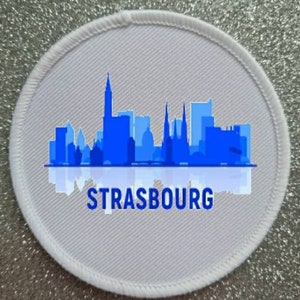 May include: White round patch with a blue silhouette of the Strasbourg skyline and the word "STRASBOURG" in blue text.