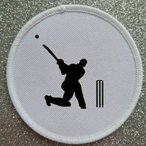 May include: White round patch with a black silhouette of a cricket player batting with a ball in the air and a set of stumps behind the player.