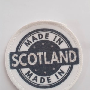 May include: White round patch with black text that reads "Made in Scotland Made in" with five stars around the text.