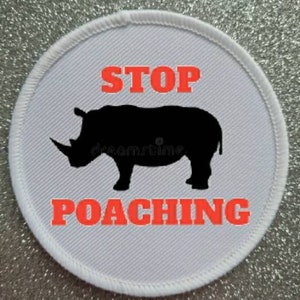 Könnte beinhalten: Ein weißer runder Aufnäher mit rotem Text, der "STOP POACHING" sagt, und einer schwarzen Silhouette eines Nashorns.