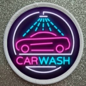 Peut inclure: Un patch circulaire blanc avec un fond noir et un panneau de lavage de voiture néon rose et bleu. Le panneau représente une voiture avec une douche d'eau au-dessus et le texte "CARWASH" en néon bleu et rose.