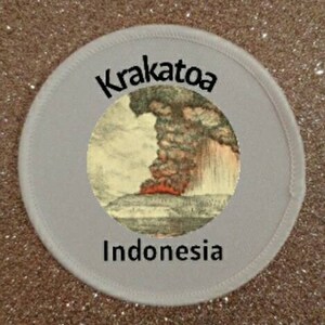 May include: A white round patch with black text that reads "Krakatoa Indonesia" and a black and white illustration of a volcanic eruption with a large plume of smoke.