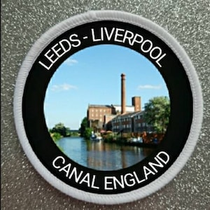 May include: White round patch with black border and white text that reads "Leeds - Liverpool Canal England". The patch features a photo of a canal with a brick building in the background.