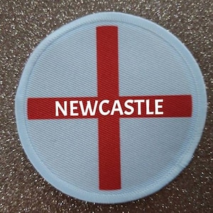 May include: A white round patch with a red cross and the word "NEWCASTLE" in the centre.