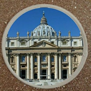 May include: A circular image featuring St. Peter's Basilica in Vatican City, framed by a glittery, gold-toned border. The basilica's dome and facade are visible against a clear blue sky. The building has columns and statues.