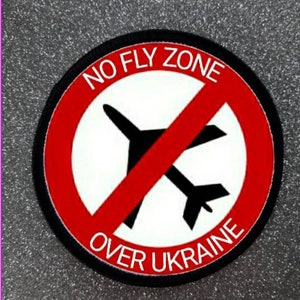 Könnte beinhalten: Ein roter Kreis mit einer diagonalen roten Linie durch eine schwarze Flugzeugsilhouette. Der Kreis trägt den Text "NO FLY ZONE OVER UKRAINE" in weiß.