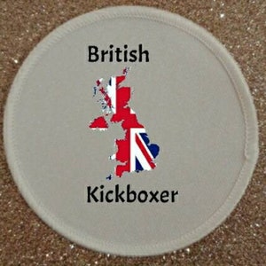 Puede incluir: Un parche redondo blanco con fondo gris. El parche presenta un mapa del Reino Unido con el diseño de la bandera de la Union Jack. El texto "British Kickboxer" está impreso debajo del mapa.