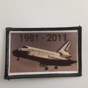May include: A black and white patch with a space shuttle and the text "1981 - 2011" on a brown background.