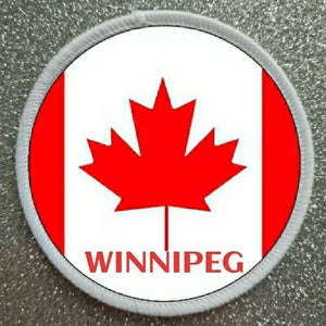 May include: A white and red circular patch with the Canadian flag and the word "WINNIPEG" in red letters.