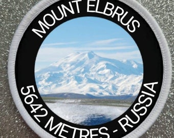 Peut inclure: Un écusson rond blanc et noir avec une photo du mont Elbrouz, une montagne enneigée en Russie. Le texte "MOUNT ELBRUS 5642 METRES - RUSSIA" est imprimé autour de la photo.