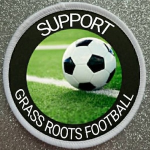 May include: White round patch with black text that reads "Support Grass Roots Football" and a black circle with a white soccer ball in the center.
