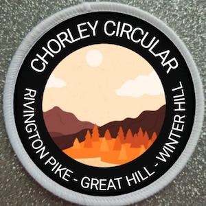 May include: A black and white circular patch with the text "Chorley Circular Rivington Pike - Great Hill - Winter Hill" around the edge. The centre of the patch features a stylised illustration of a landscape with mountains, trees, and a sun.