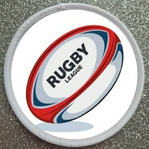 Puede incluir: Parche redondo blanco con una pelota de rugby roja, blanca y azul. La pelota tiene el texto "RUGBY LEAGUE" en ella.